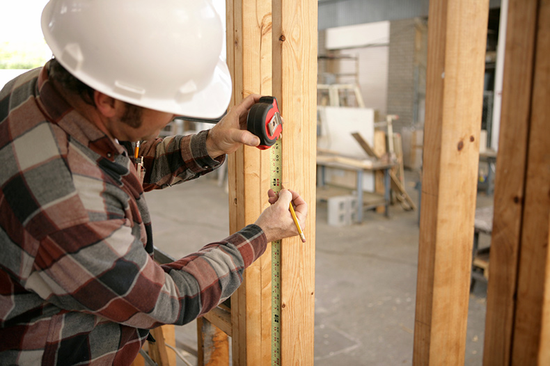 A construction electrician measuring up 48 inches to install a switch box.